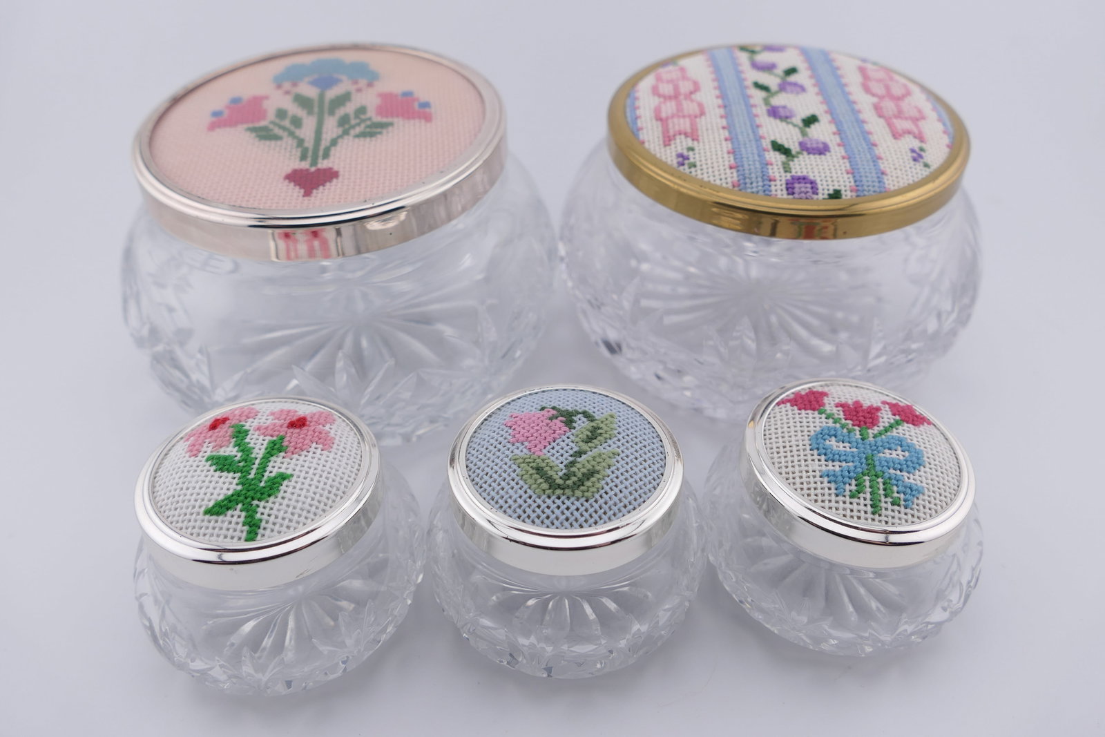 Five Custom Needlepoint and Crystal Trinket Boxes: Five crystal trinket boxes featuring custom needlepoint lids in motifs such as flowers and ribbons. One is marked on the bottom Tudor, England. Excellent condition. Size: Largest 3.5"dia x 2.25"h