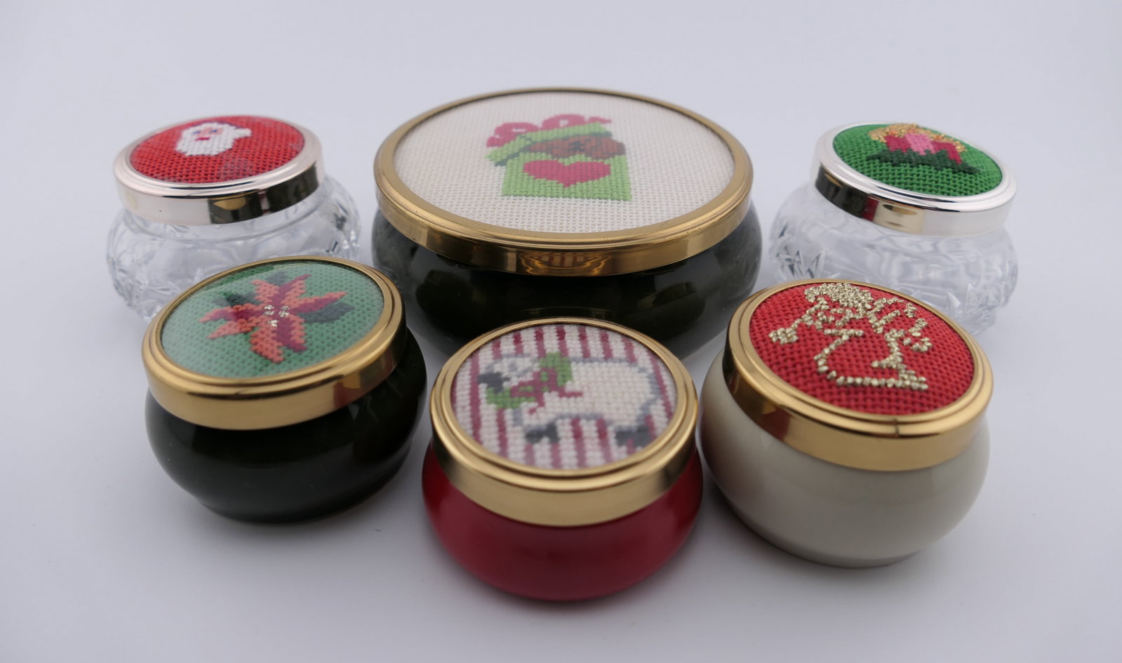 Six Custom Christmas Needlepoint Trinket Boxes: Six small trinket boxes with custom needlepoint lids in Christmas motifs such as a dog in a gift box, candles, a wreath, angel, poinsettia blossom, and more. Basins include ceramic, and two crystal.