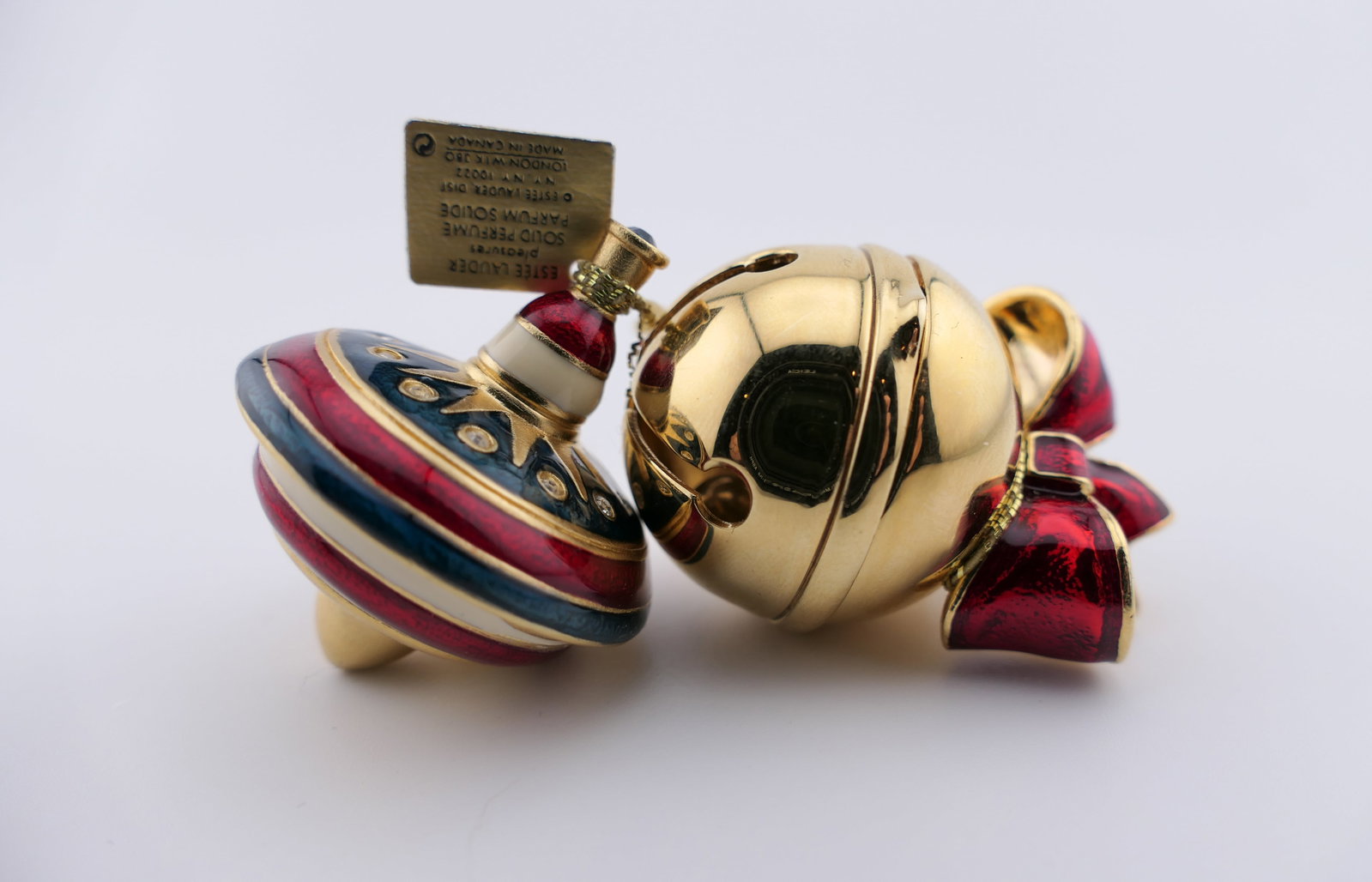 Two Estee Lauder Christmas Perfume Compacts: Two Estee Lauder solid perfume compacts in Christmas designs including a Jingle Bell (2007), and a Spinning Top (2006), both embellished with glass rhinestones. Compacts contain solid perfume in the