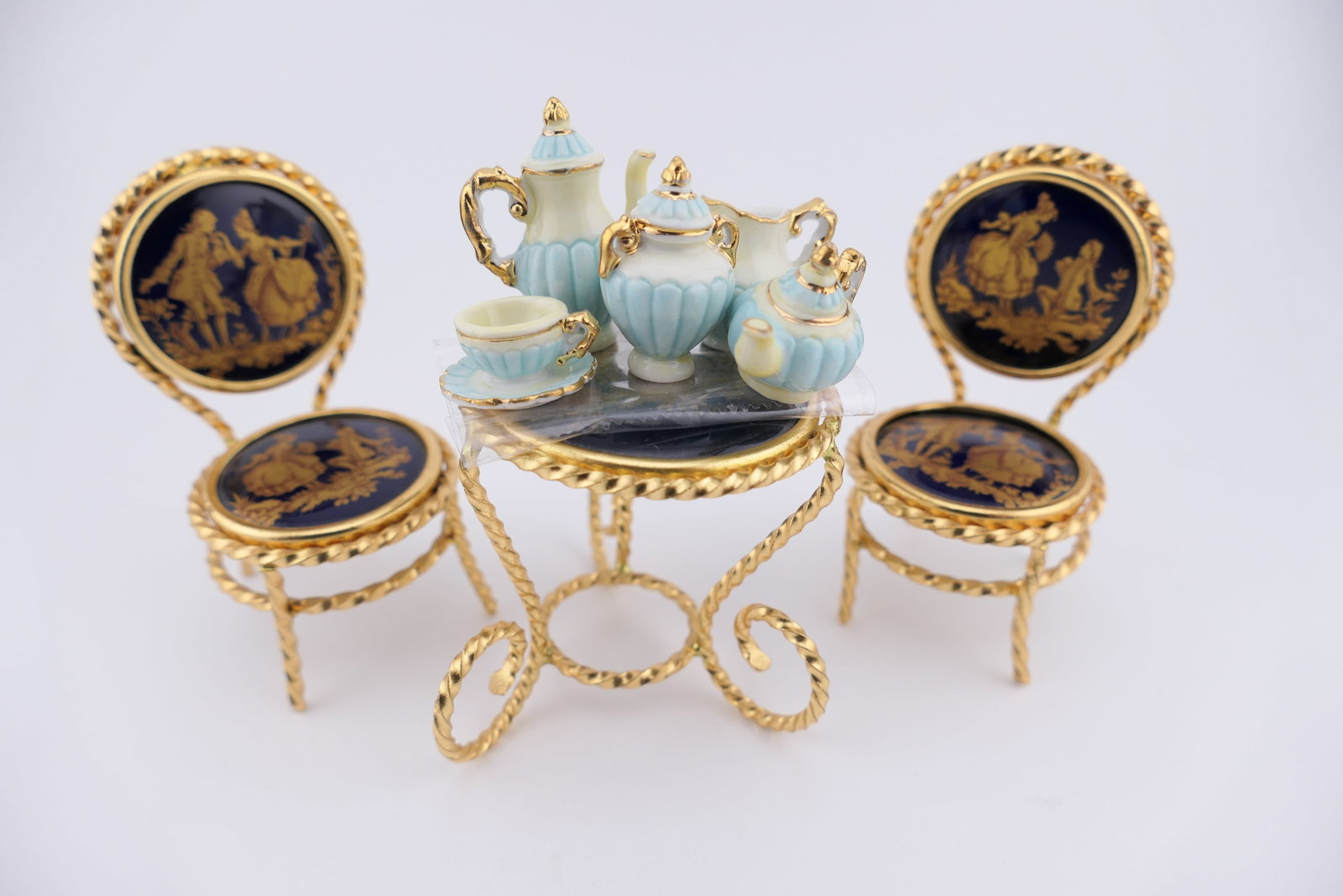 Miniature Bistro Table and Tea Set: Marked Limoges miniature bistro table and chairs with porcelain seats and backs accented in dark blue with gilt rococo style details in a twisted gold tone frame, alongside a Laduree Paris miniature t