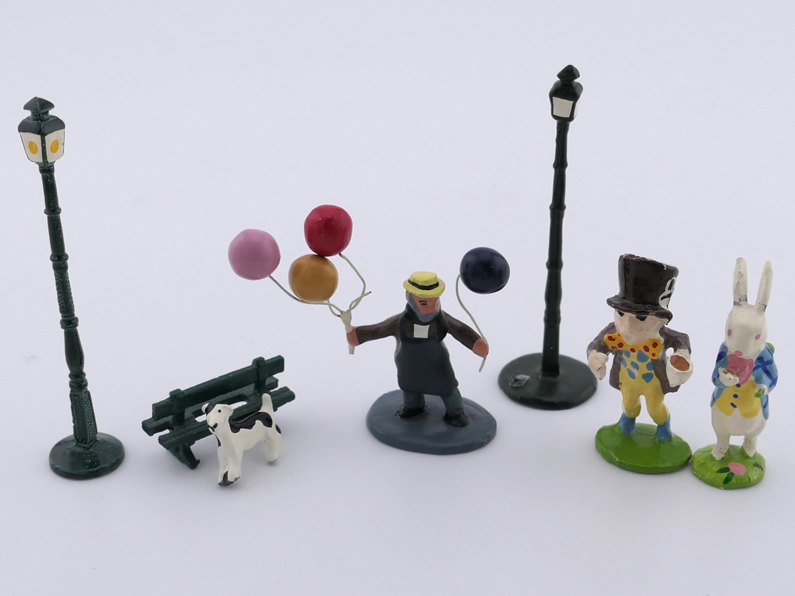 Hand Painted Miniature Figurines: Hand painted miniature figurines in the style of J. Carlton by Gualt, including two lamp posts, a balloon man, a mad hatter and rabbit, and a dog and bench. Excellent condition. Size: 1"h Location:
