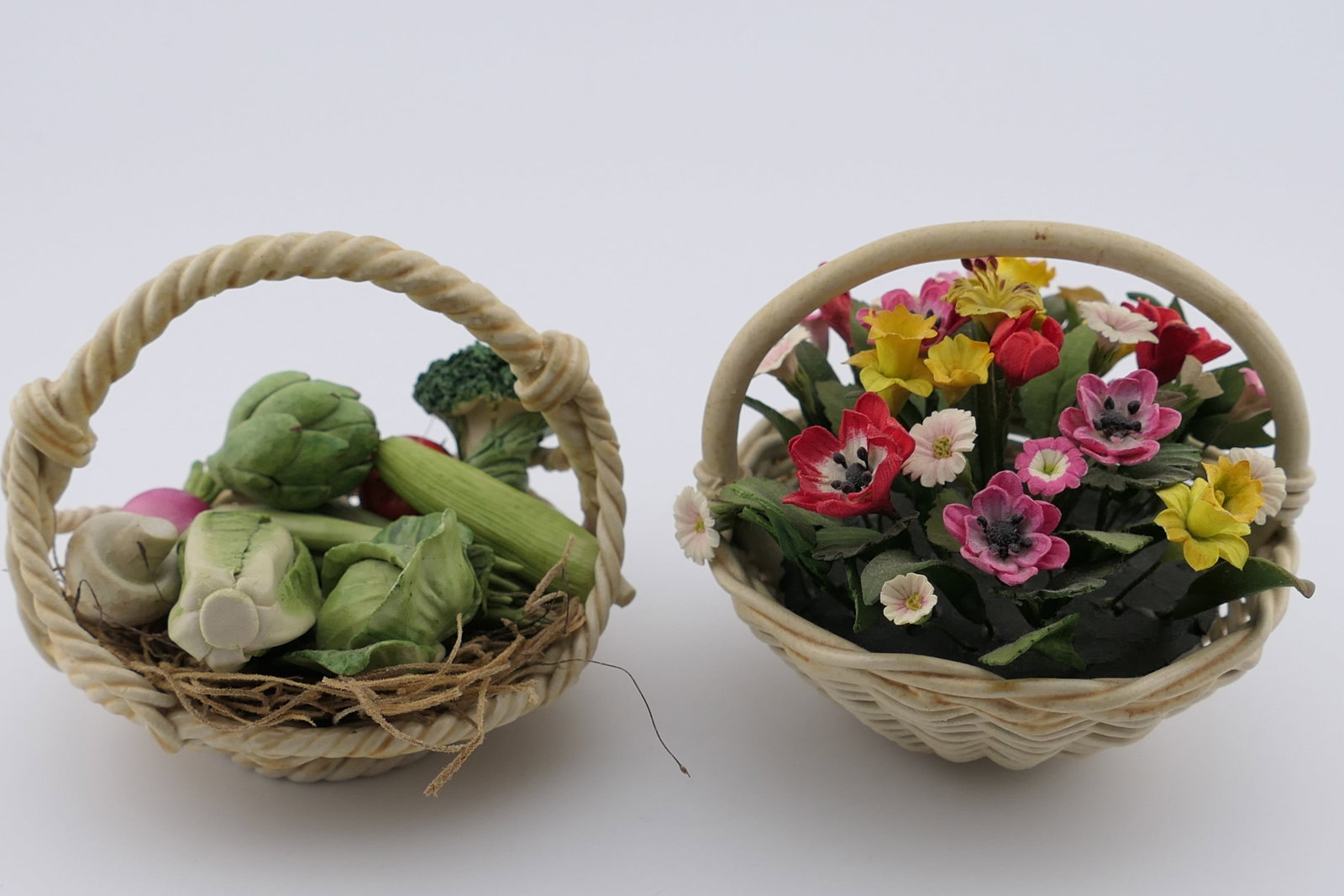 Flower and Vegetable Basket Accents: Two accent figurines including one in porcelain depicting a bushel of vegetables with realistic hand painted details, alongside a composite flower bouquet containing multicolored blooms. The