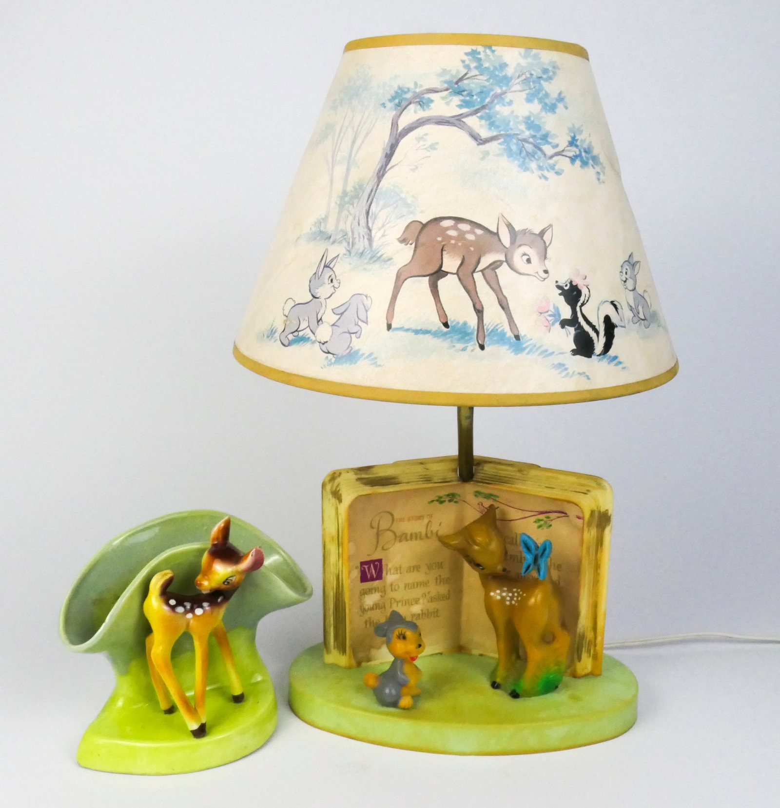 Vintage Bambi Lamp and Planter: Bambi themed table lamp by The Dolly Toy Co. featuring plastic base with storybook design and paper shade with illustrated scene (water damage on storybook and staining on shade), lights. Plus a