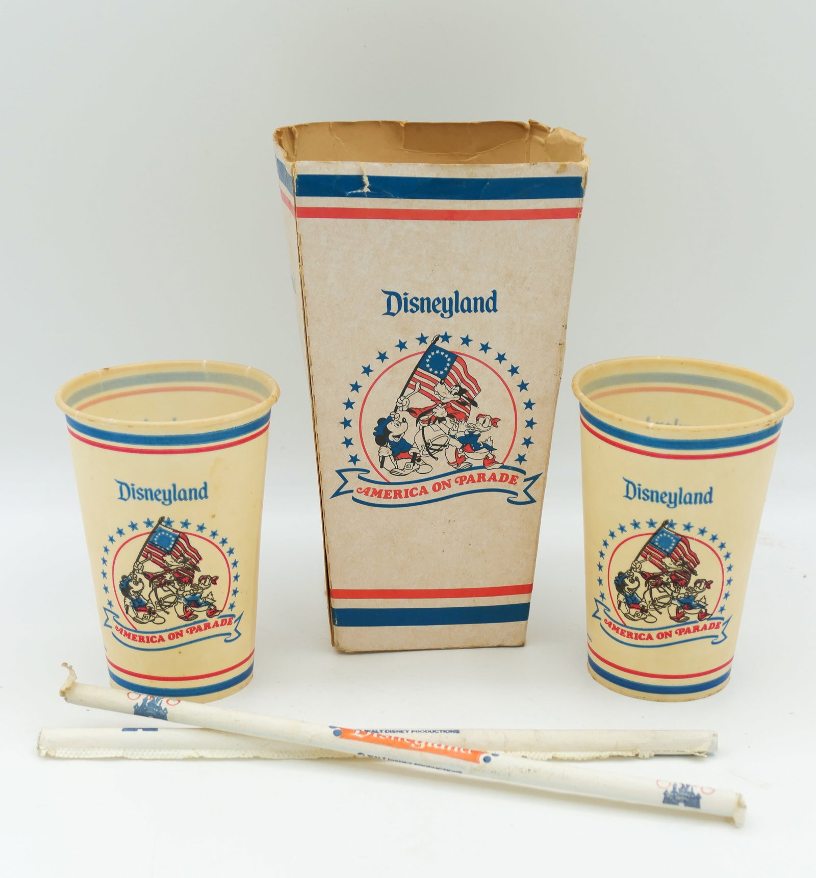 Disneyland America on Parade Popcorn Bucket and More: 1975-1976 Disneyland America on Parade Bicentennial popcorn box, cups and straws. All show age discoloration. Paper on straws is nearly worn off. Size: Bucket 3.5"w x 4"d x 6.5"h