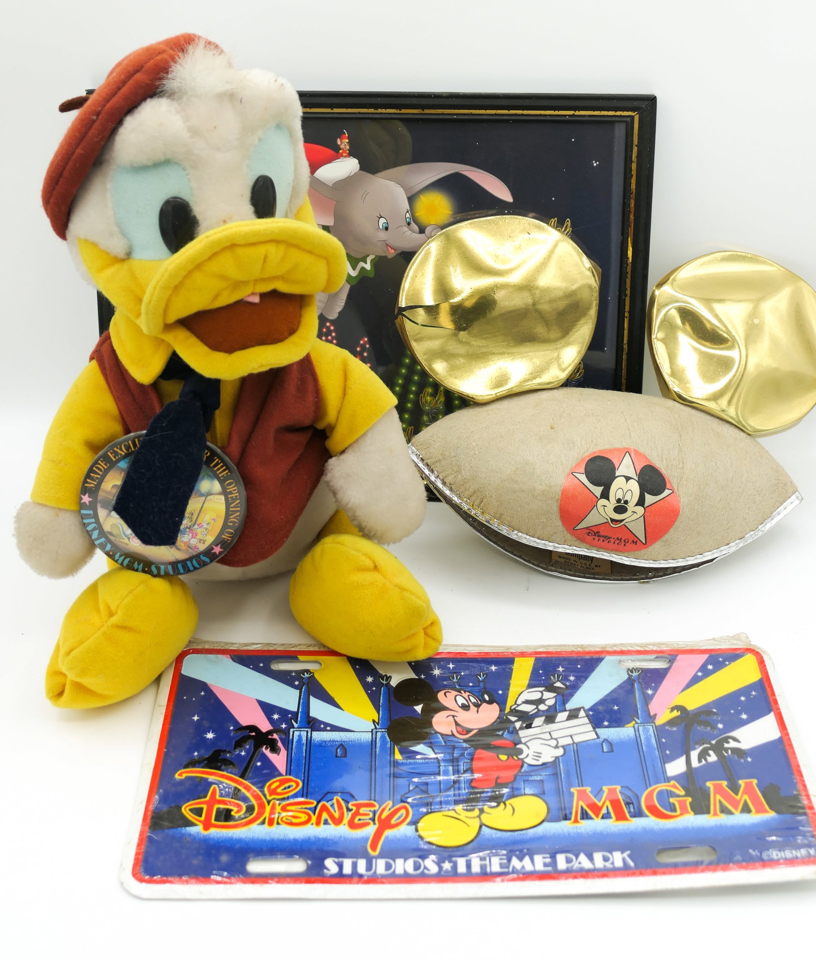 Disney MGM Studio Park Memorabilia: Disney MGM Studio park memorabilia including Mickey ears MGM hat, Donald Duck plush figure with button made exclusively for Disney MGM Studio opening, MGM license plate new in plastic and a framed
