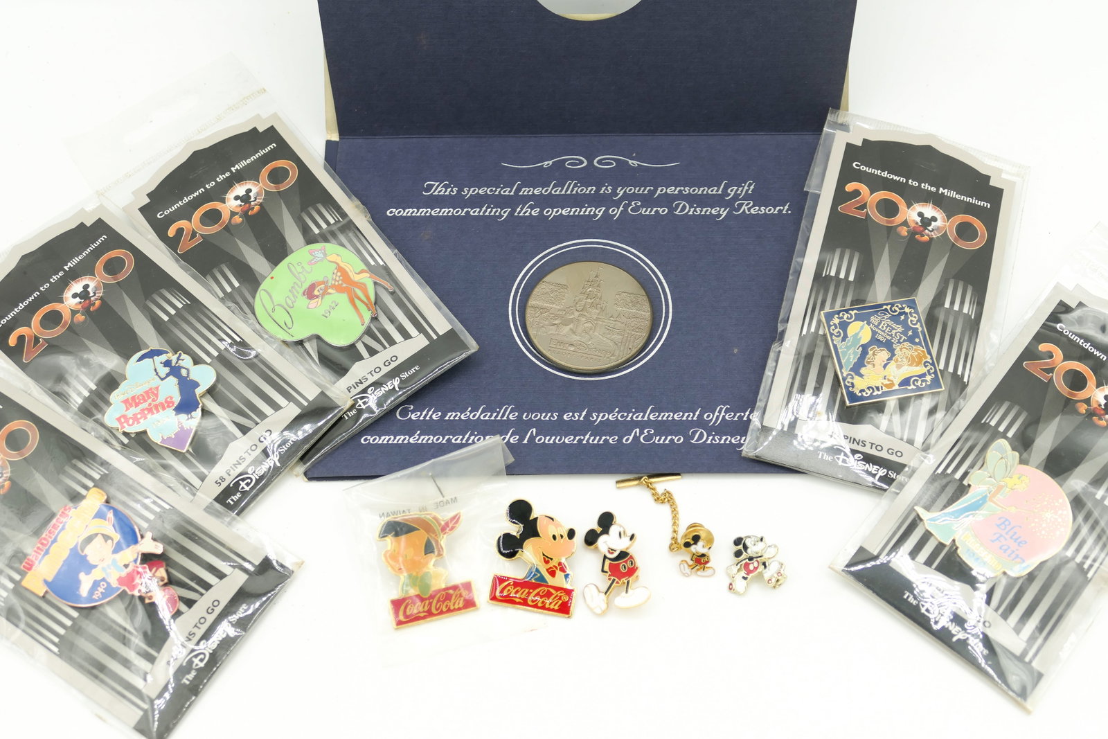 Disney Collectible Pins and Coin: Ten Disney collectible pins including 5 "Countdown to the Millennium" pins with different characters on each one, 3 Mickey Mouse and 2 Coca-Cola pins. Also includes a Euro Disney Resort coin.
