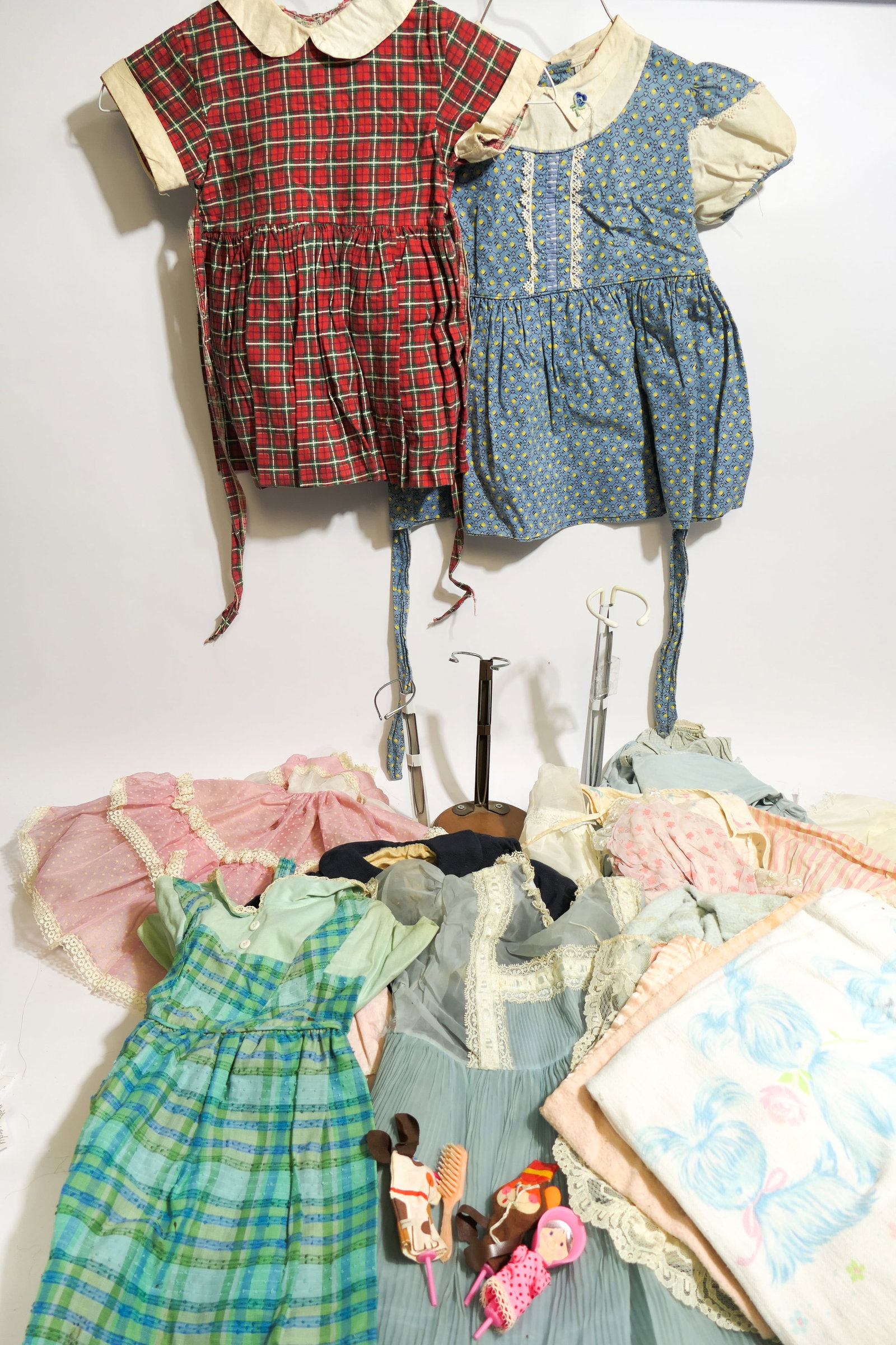 Doll Clothing and Stands: Assortment of doll clothing in multiple sizes and conditions, plus three stands and accessories. Wear, and slight smell from age is present.