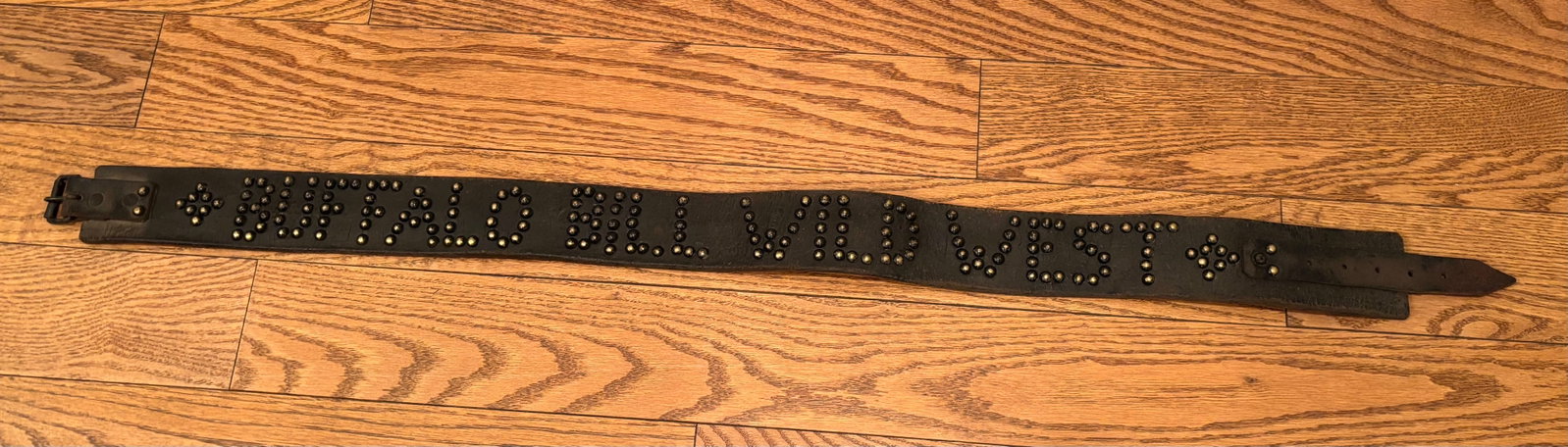 Tacked Leather BUFFALO BILL WILD WEST Belt: An old Tacked leather belt spelling out BUFFALO BILL WILD WEST, with some tacked designs at each end. It has its old iron buckle and leather tongue at ends. The brass tacks are in a heavy leather