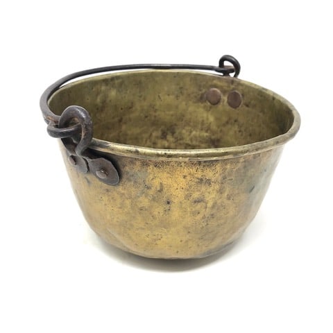 Small Brass Indian Trade Kettle: A nice small size brass Indian trade kettle with hand forged iron looped ears having penny “feet”, secured by large copper rivets. It has a rolled rim, and shows early spaced lathe turning mar