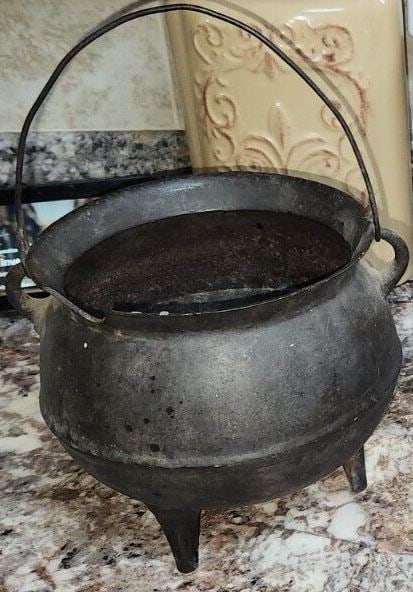 C.W. Era Cast Iron Pot, Bulbous Shape: A cast iron pot, bulbous shape, rounded ears, 3 legs, and a pouring “gate ‘ line on the bottom. circa. 19th century, Civil War era. The rim has an old chip and the wire handle is a replacement han