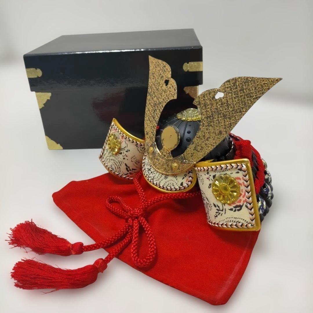 Miniature Gold Samurai Helmet Ornament: This is a miniature samurai helmet ornament, traditionally displayed during the Boys' Festival (Tango no Sekku). The golden kuwagata ornament is striking, combined with a red fabric base, creating a s