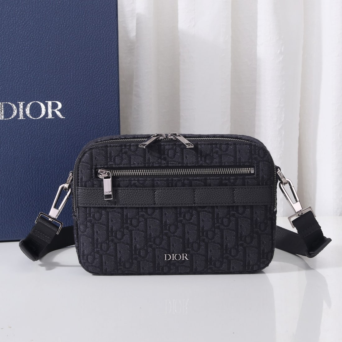 Christian Dior: The Safari messenger bag is practical and compact, perfect for everyday carry. Crafted from black Oblique printed fabric with black grained calfskin details, it features a zippered compartment and fro