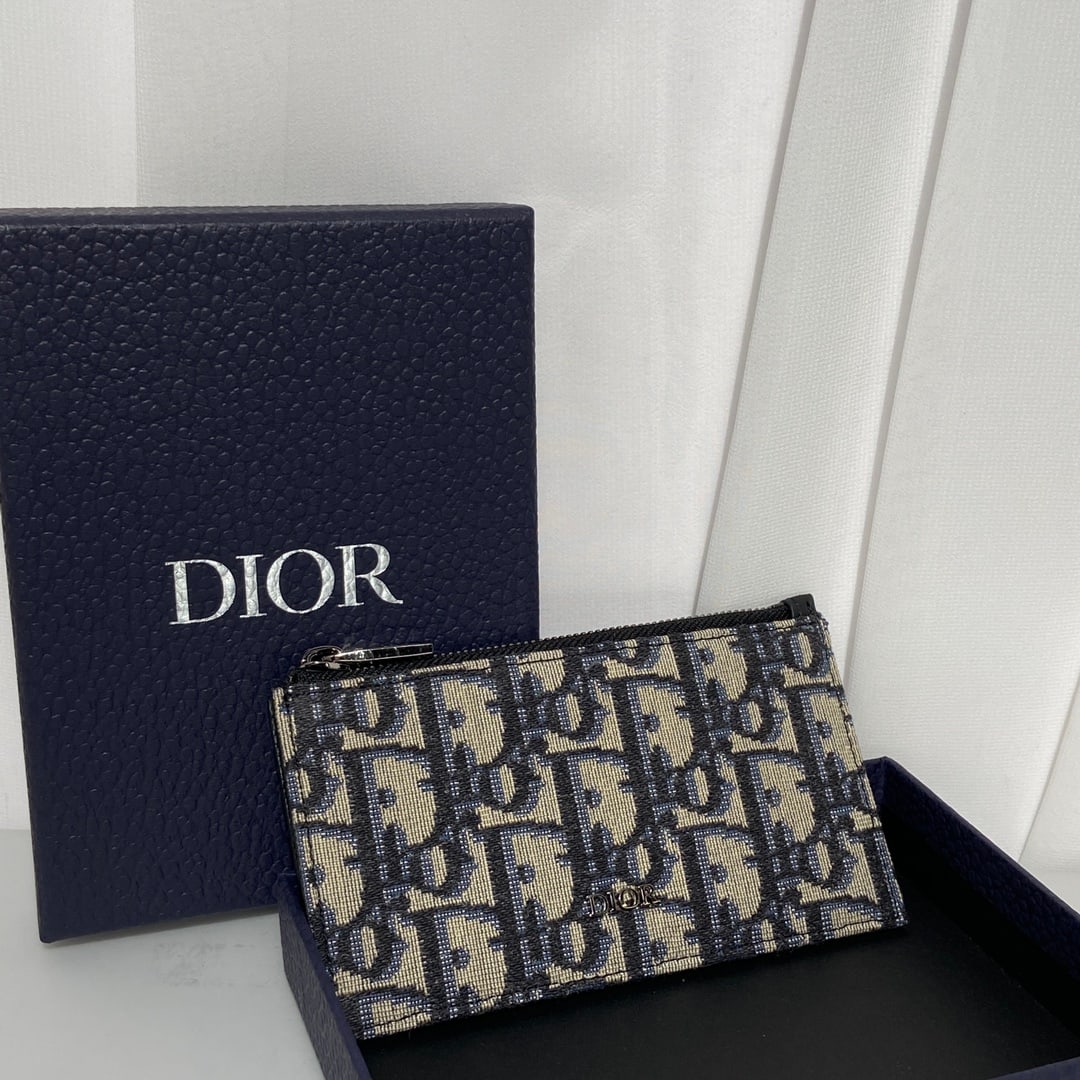 Christian Dior: This DIOR cardholder features a refined and elegant zippered design. Crafted from Oblique printed fabric, it's finished with tonal grained calfskin and the DIOR logo. It includes a zippered gusseted c