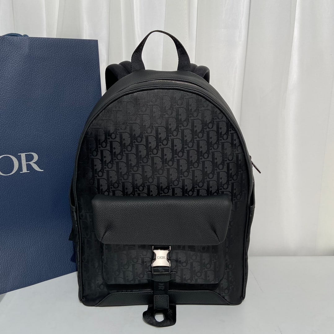 Christian Dior: The Dior Explorer backpack is crafted from black technical fabric, adorned with the Oblique Mirage print and black grained calfskin leather, featuring distinctive DIOR leather patches on the sides. Th