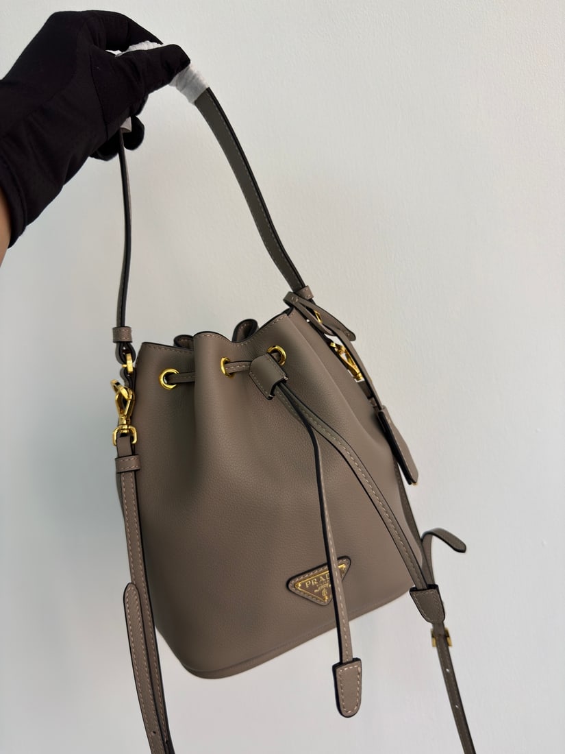 PRADA bucket bag: This stylish mini bucket bag features a soft bucket shape, adorned with delicate gold-plated hardware and the iconic triangular logo. Made of leather, it includes an adjustable shoulder strap for adde