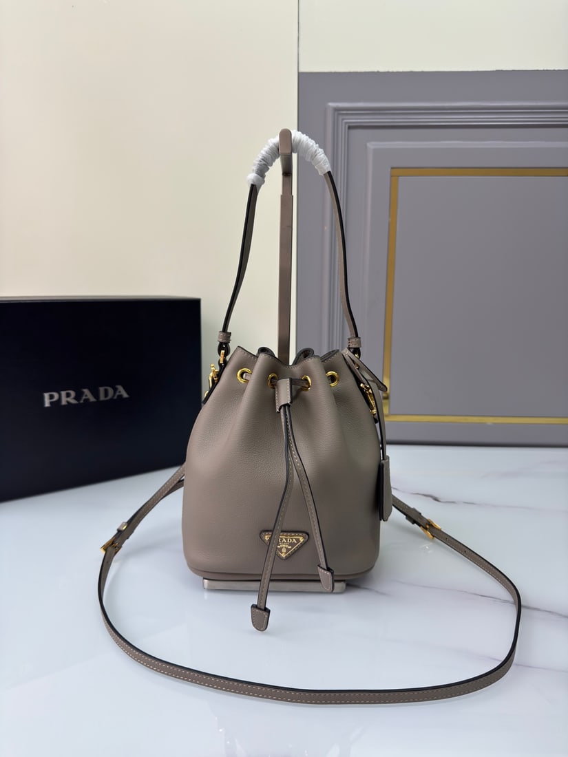 PRADA bucket bag: This stylish mini bucket bag features a soft bucket shape, adorned with delicate gold-plated hardware and the iconic triangular logo. Made of leather, it includes an adjustable shoulder strap for adde