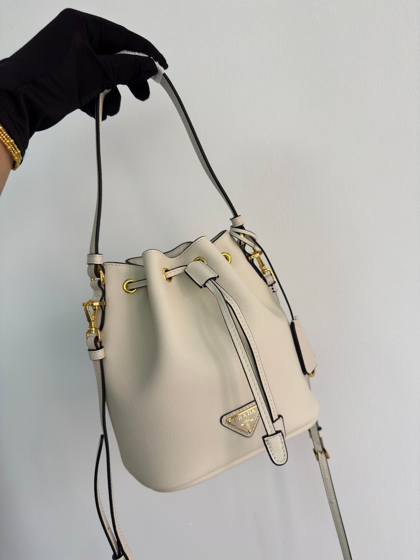 PRADA bucket bag: This stylish mini bucket bag features a soft bucket shape, adorned with delicate gold-plated hardware and the iconic triangular logo. Made of leather, it includes an adjustable shoulder strap for adde