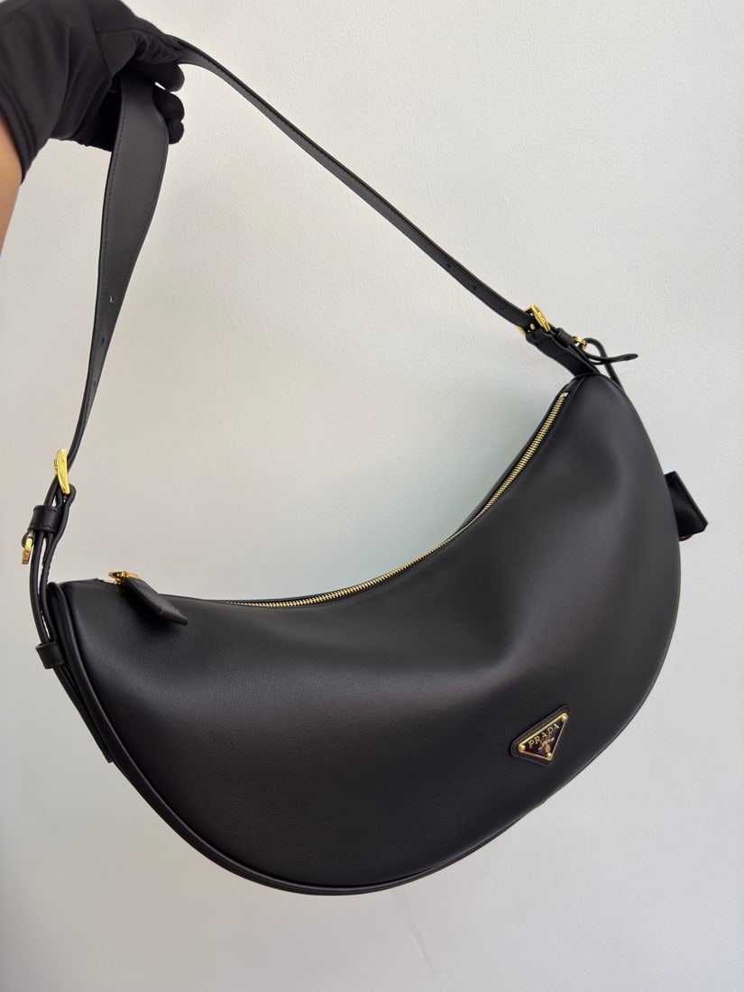 PRADA underarm bag: This leather underarm bag features a soft and lightweight design, offering a fresh interpretation of the classic crescent shape. Its elegant curves accentuate its oversized silhouette, creating a spac