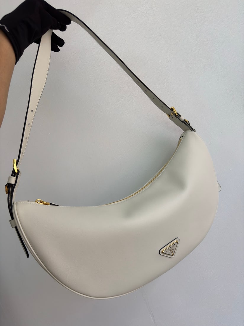 PRADA underarm bag: This leather underarm bag features a soft and lightweight design, offering a fresh interpretation of the classic crescent shape. Its elegant curves accentuate its oversized silhouette, creating a spac