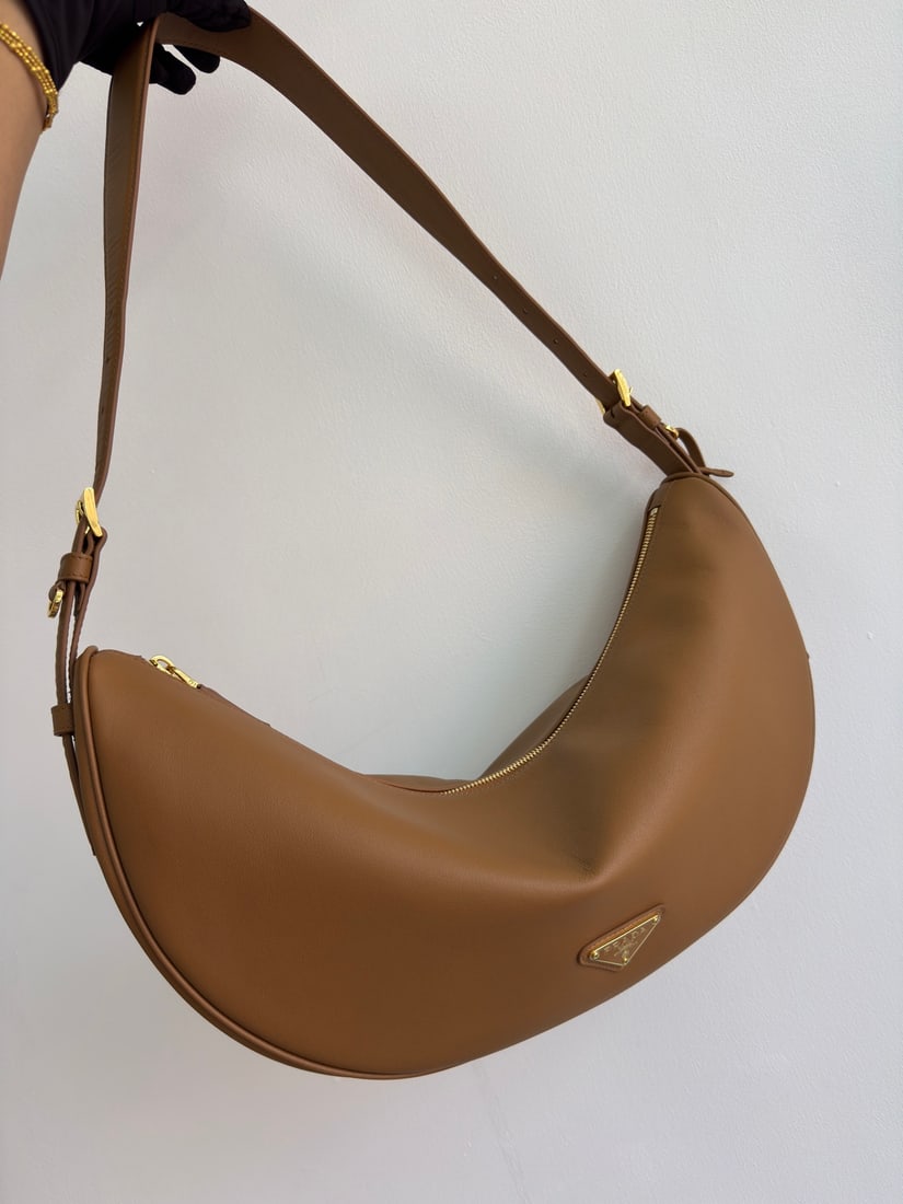 PRADA underarm bag: This leather underarm bag features a soft and lightweight design, offering a fresh interpretation of the classic crescent shape. Its elegant curves accentuate its oversized silhouette, creating a spac