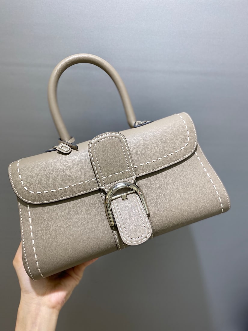Delvaux brillant: Delvaux brillant, a Belgian royal warrant holder with a creamy grey exterior, exudes understated luxury with semi-hand-stitched waxed thread. Comes with an adjustable shoulder strap and a mirror. Lamb