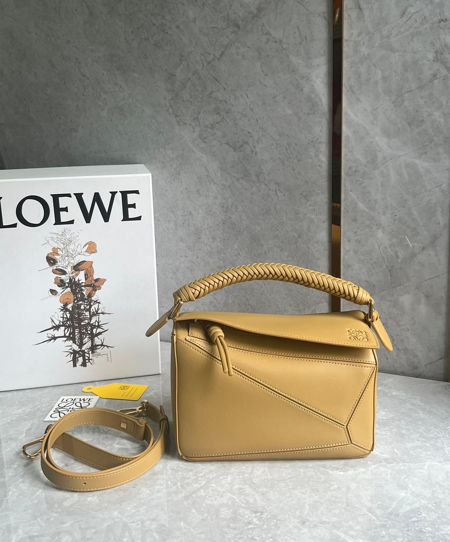 LOEWE: The LOEWE woven handle puzzle is crafted from supple calfskin. The heavily woven handle and knotted zipper design exude a premium feel, while the suede lining adds a touch of luxury. Size: 24 x 10 x 1