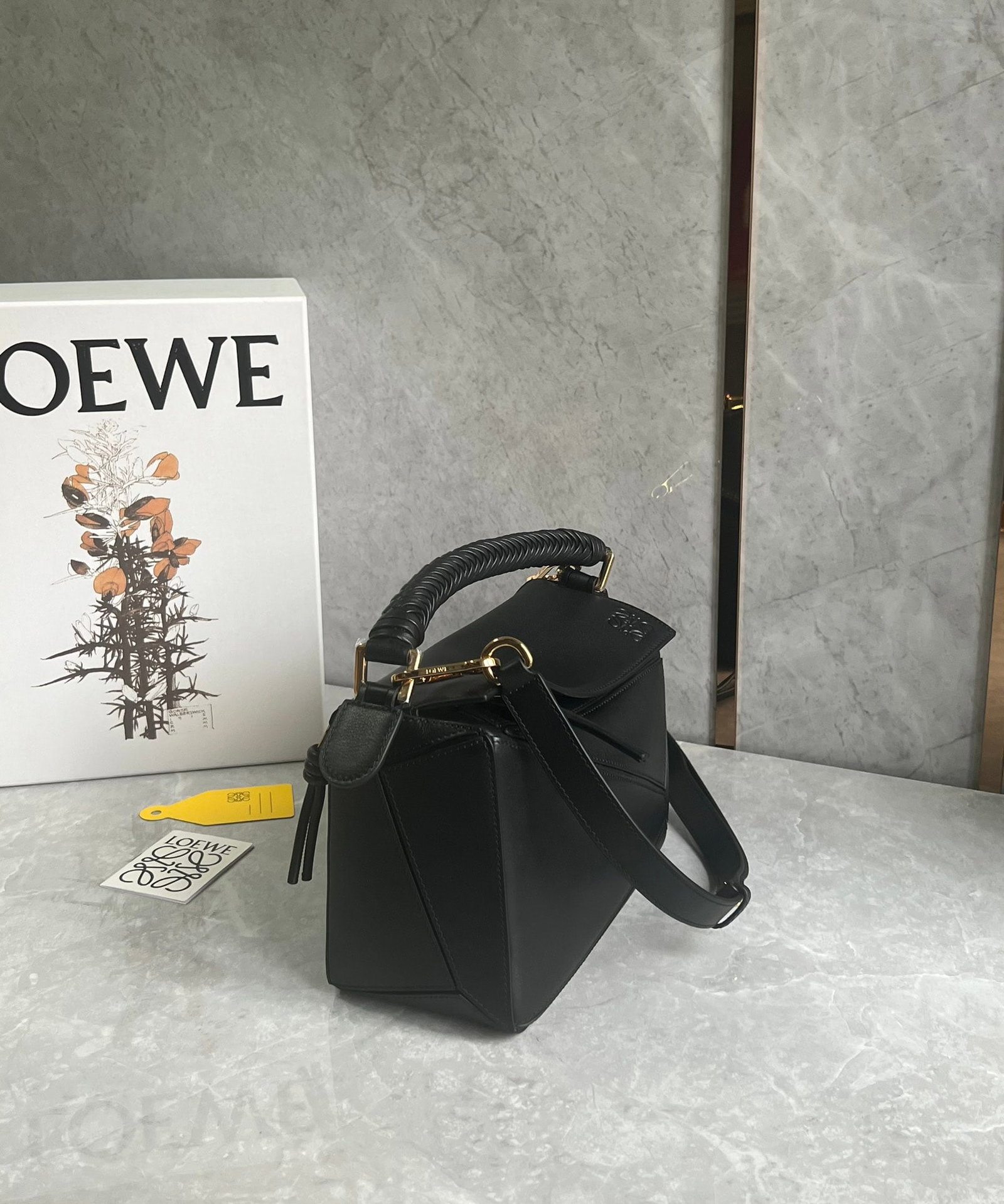 LOEWE: The LOEWE woven handle puzzle is crafted from supple calfskin. The heavily woven handle and knotted zipper design exude a premium feel, while the suede lining adds a touch of luxury. Size: 24 x 10 x 1