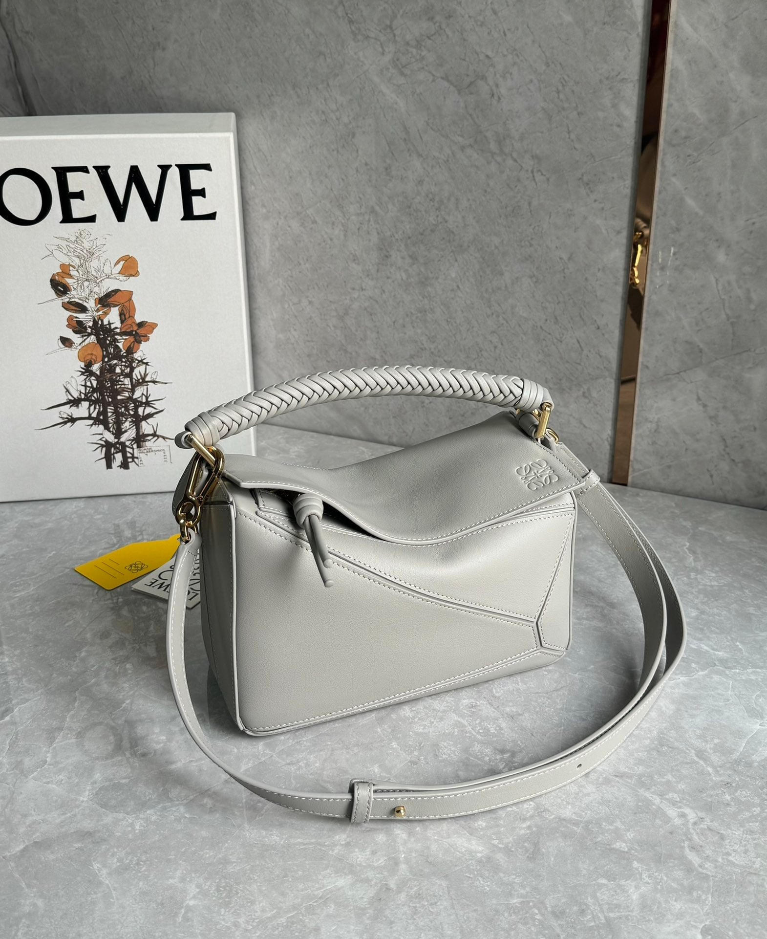 LOEWE: The LOEWE woven handle puzzle is crafted from supple calfskin. The heavily woven handle and knotted zipper design exude a premium feel, while the suede lining adds a touch of luxury. Size: 24 x 10 x 1