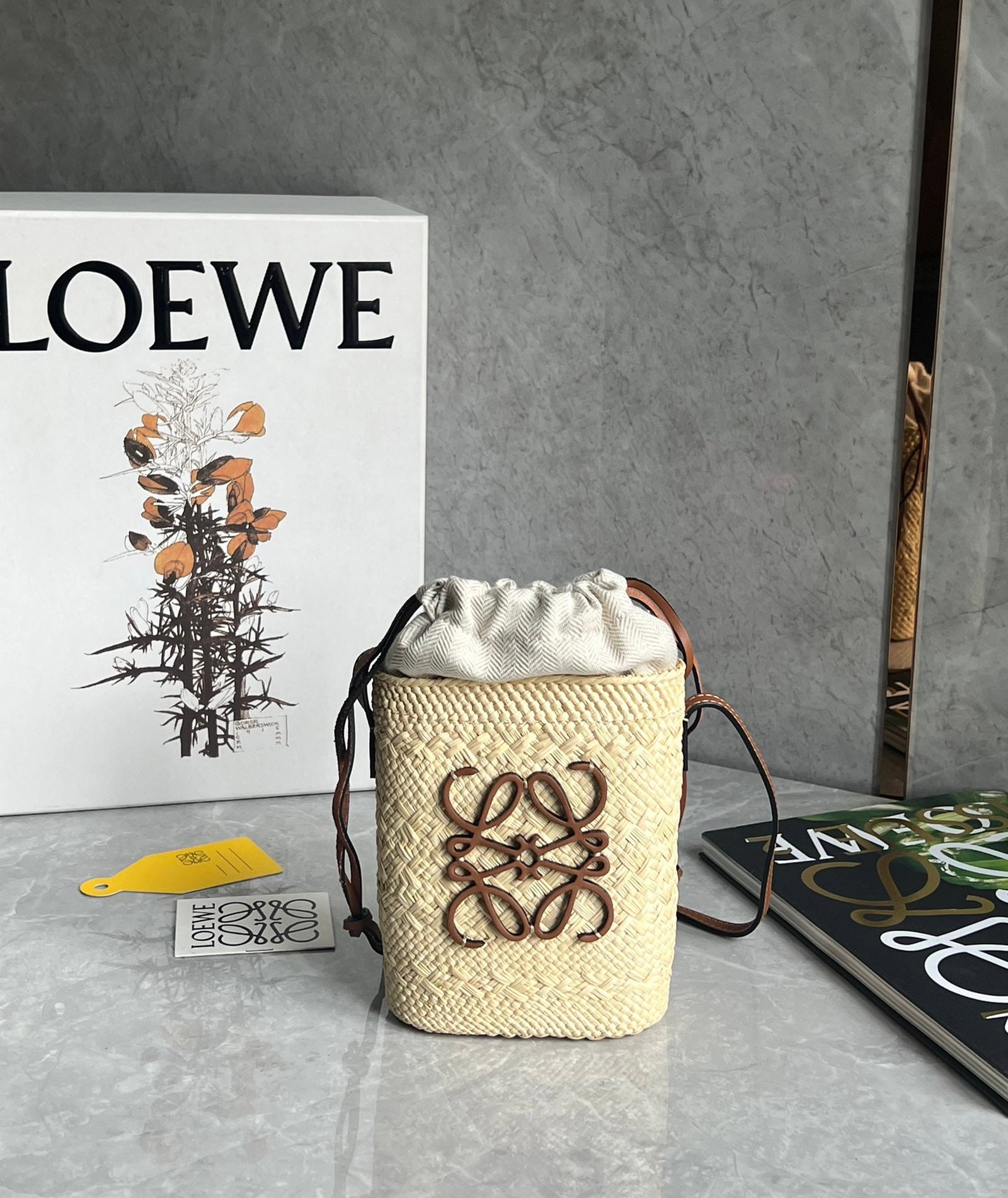 LOEWE: LOEWE Anagram Basket is a handmade raffia woven bag with a large capacity. It features a non-removable inner pouch for easy storage, and a drawstring closure to prevent small items from falling out.