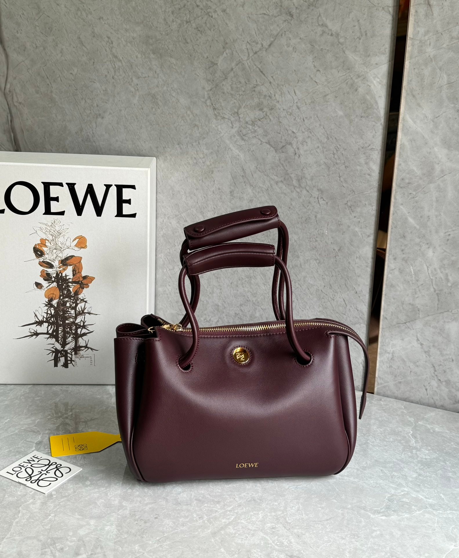 LOEWE: The LOEWE Small Madrid bag boasts a sculpted, structured trapezoidal shape with a gusseted design, adjustable handles, and a Pebble magnetic closure. Made from supple cowhide leather, it features a pr