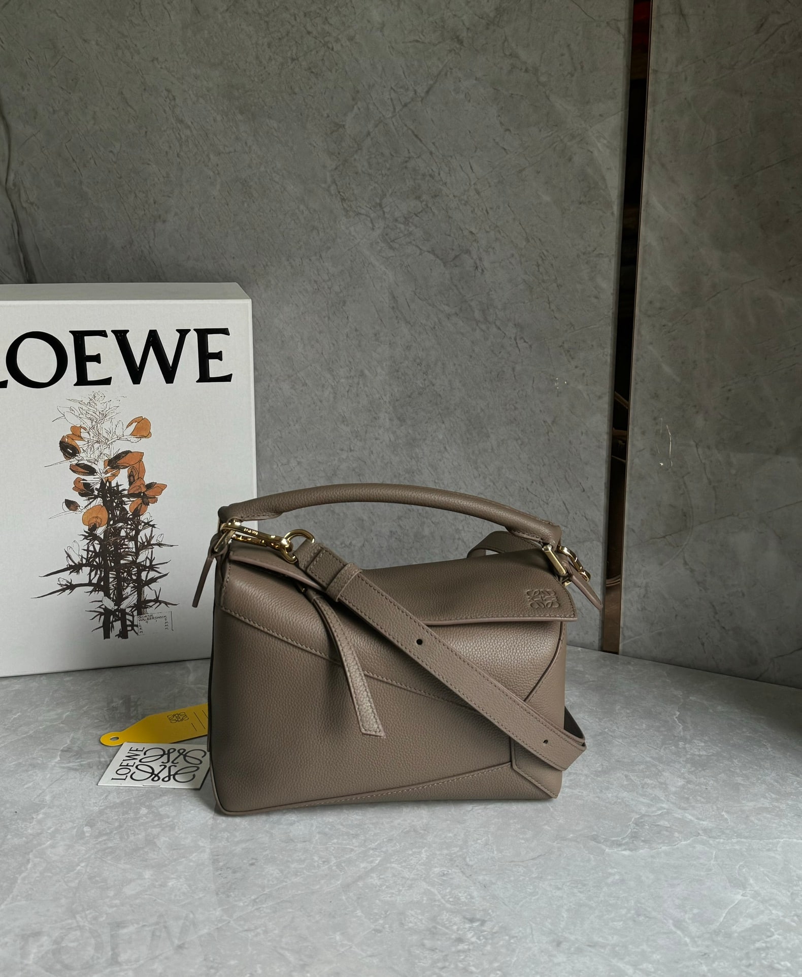 LOEWE: The LOEWE Puzzle bag, in a greyish-brown color, is made of pebbled cowhide. The entire bag is constructed from pebbled leather panels, making it lightweight yet surprisingly spacious. Practical, versa