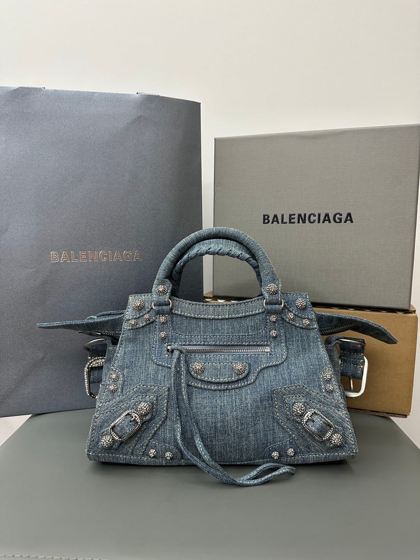 Balenciaga neo cagole motorcycle bag in denim blue: The neo cagole motorcycle bag in denim blue with rhinestones has a particularly large capacity; it can fit an umbrella or water bottle. The bag's craftsmanship is intricate. It measures 26 x 17.8 x 11