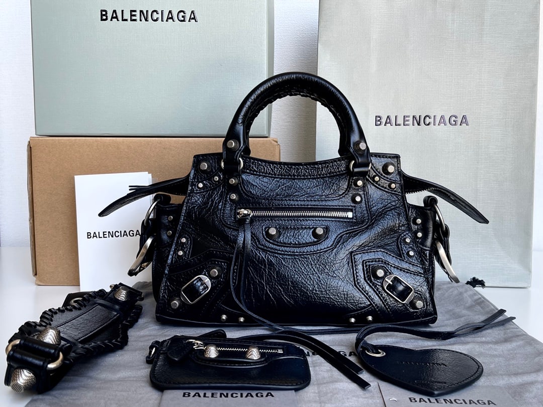 Balenciaga Neo Cagole Motorcycle Bag: This Balenciaga Neo Cagole motorcycle bag in waxed black comes with a heart-shaped mirror. Beneath its cool and edgy exterior lies a sweet heart. Carrying it instantly elevates your entire aura. A mus