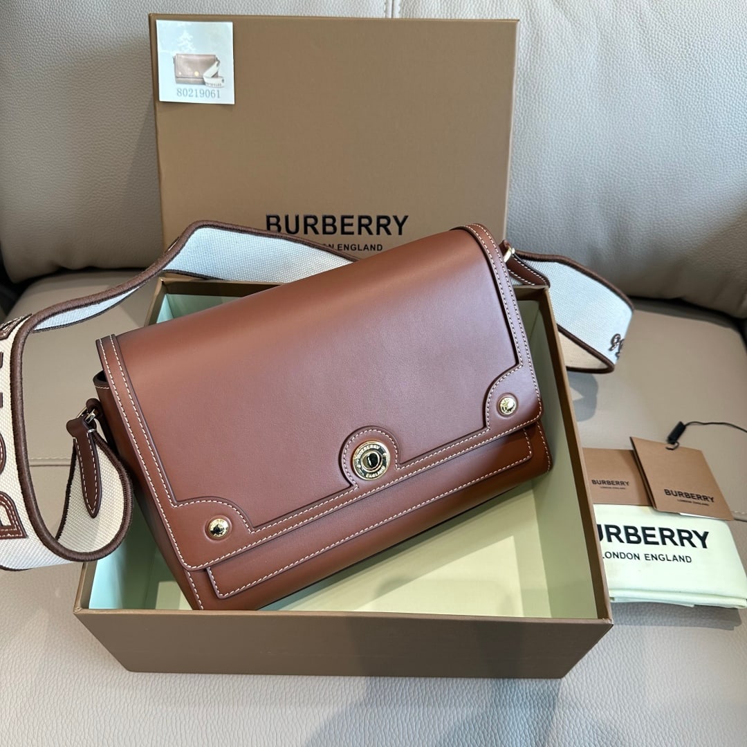 Burberry: A slim Burberry crossbody bag crafted from Italian-tanned, top-stitched leather, featuring a glossy snap closure with an engraved logo and a cotton canvas shoulder strap adorned with a Burberry monogr
