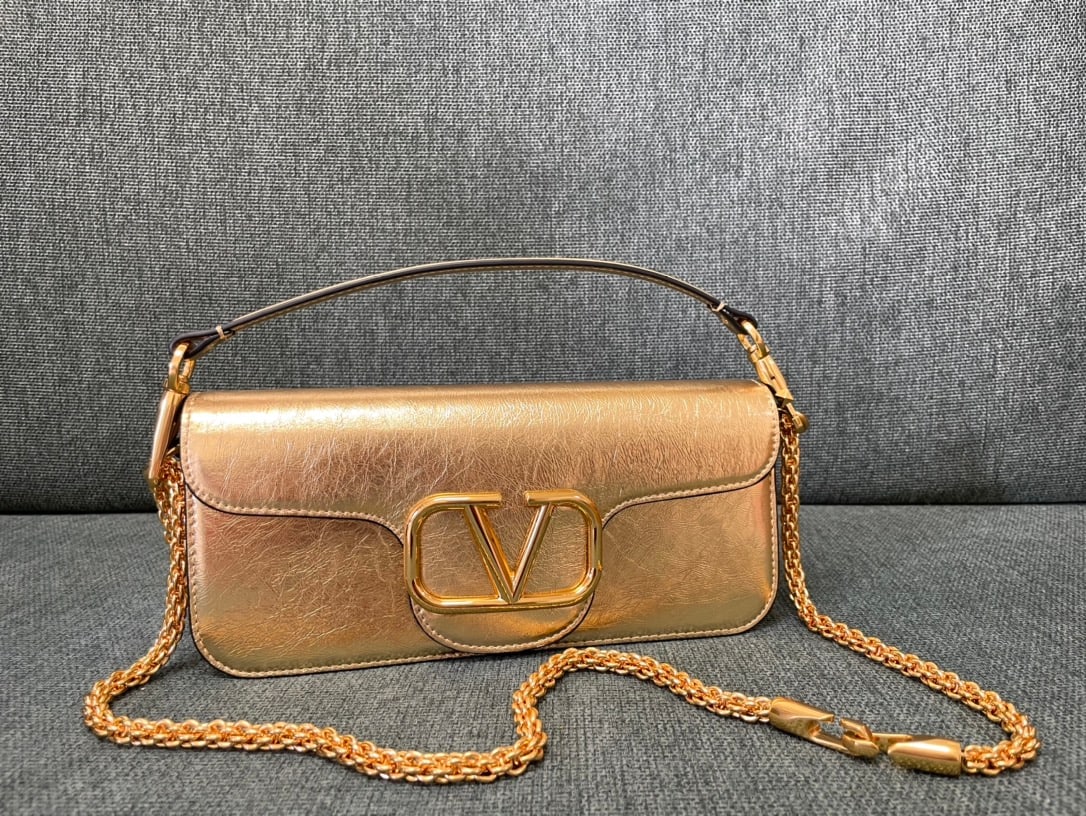 Valentino: This Valentino calfskin handbag features a papaya gold finish and a metal V-logo signacar. It can be carried on the shoulder, crossbody, or by hand, with a vintage brass finish, magnetic closure, and 