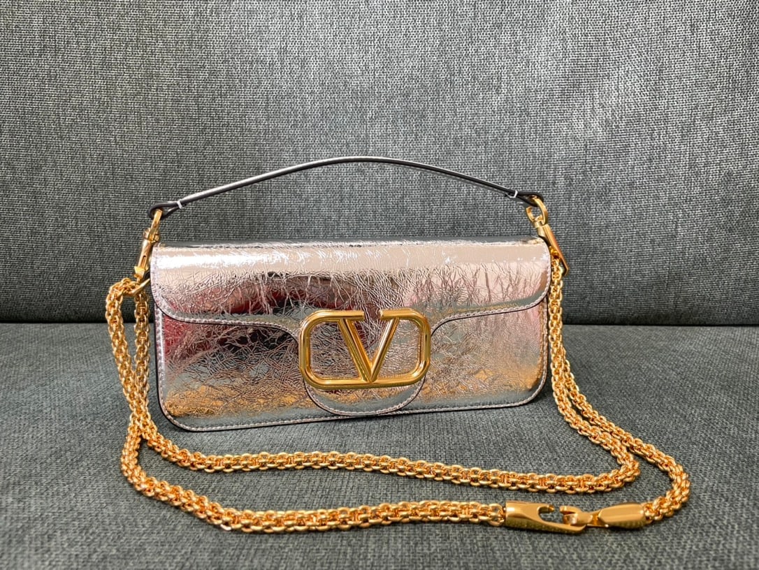 Valentino: Papaya silver Valentino calfskin handbag with metal V logo and Signacar trim - features a detachable handle and sliding chain for shoulder, crossbody, or hand carrying. Vintage brass distressed finish