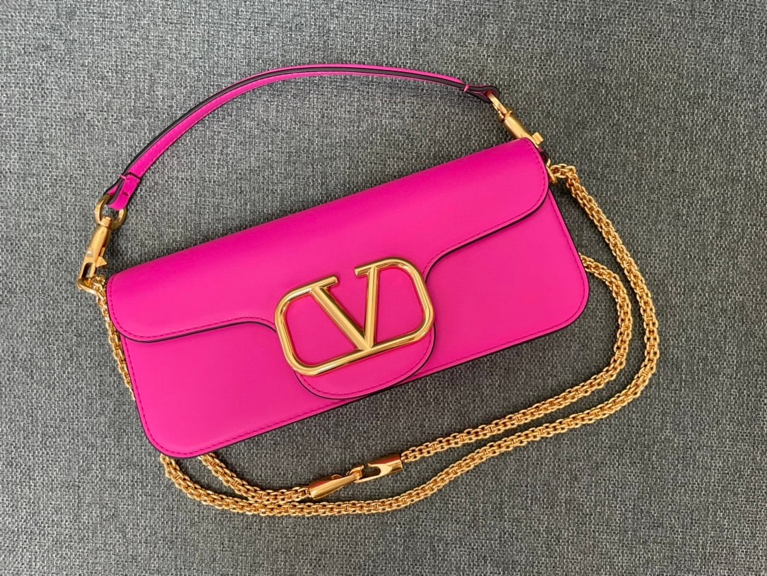 Valentino: rose-pink Valentino calfskin handbag with a metal V-logo signacar trim. Features a detachable handle and sliding chain for shoulder, crossbody, or hand carrying. Vintage brass finish hardware, magneti