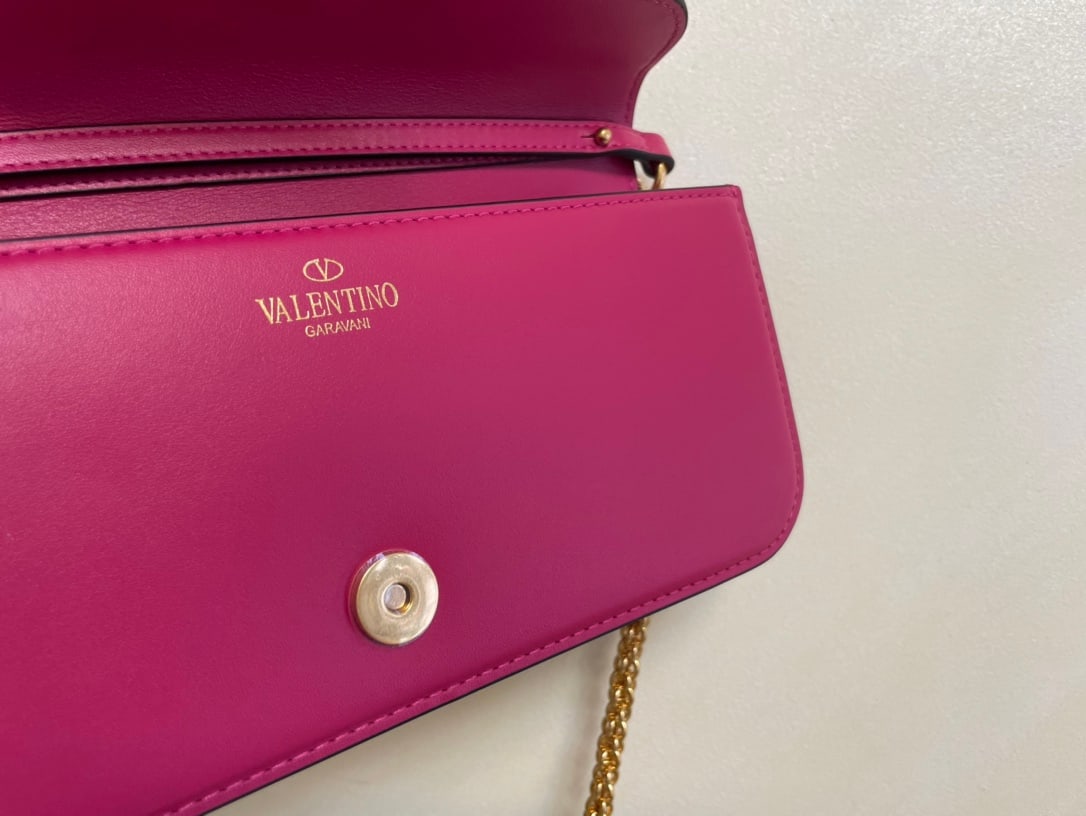 Valentino: A plum-purple Valentino calfskin handbag with a metal V-logo and Signacar design. Features a detachable handle and sliding chain for shoulder, crossbody, or hand carrying. Vintage brass finish hardwar