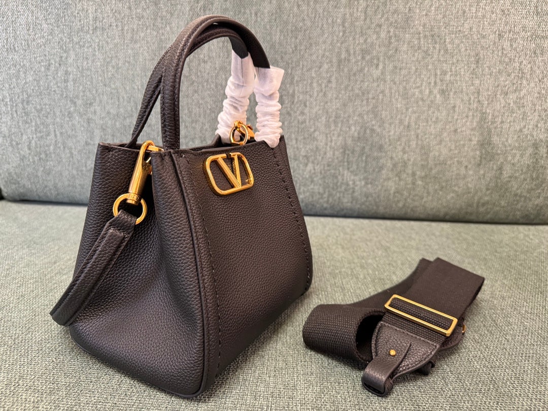 Valentino: Small black VALENTINO grained calfskin handbag with metal VLOGO SIGNATURE element. This handbag can be carried on the shoulder, crossbody, or by hand. Features include vintage brass distressed finish 