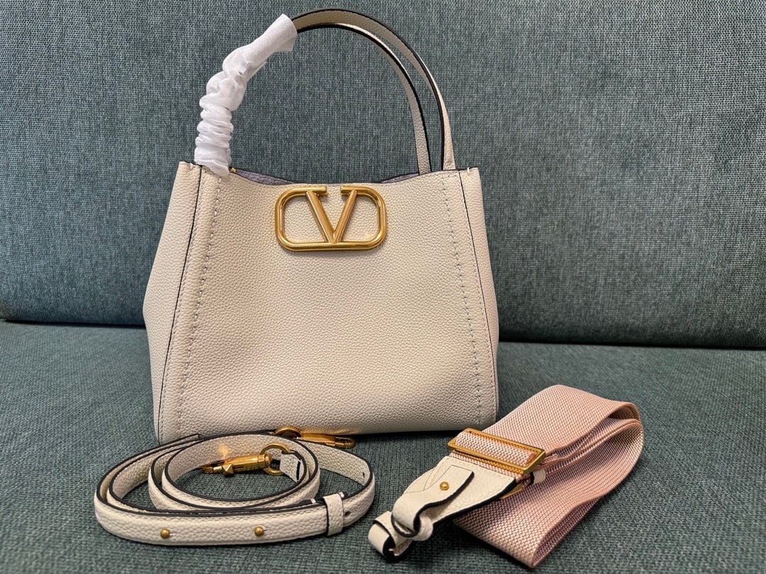 Valentino: Large off-white VALENTINO small grained calfskin handbag with metal VLOGO SIGNATURE element. This handbag can be carried on the shoulder, crossbody, or by hand. Features include vintage brass distress