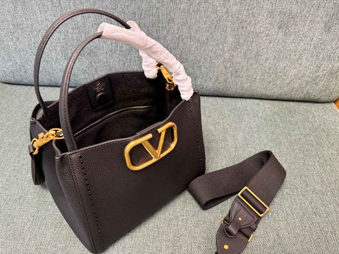 Valentino: Large black VALENTINO small grained calfskin handbag with metal VLOGO SIGNATURE element. This handbag can be carried on the shoulder, crossbody, or by hand. Features include vintage brass distressed f