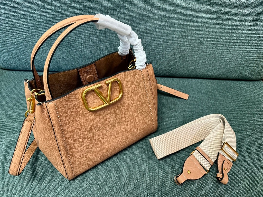Valentino: Large brown VALENTINO small grained calfskin handbag with metal VLOGO SIGNATURE element. This handbag can be carried on the shoulder, crossbody, or by hand. Features include vintage brass distressed f