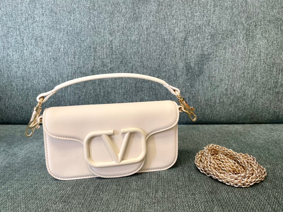 Valentino: White-edged Valentino calfskin handbag with metal V-logo and Signacar closure. Features a detachable handle and sliding chain for shoulder, crossbody, or hand carrying. Vintage brass finish, magnetic 