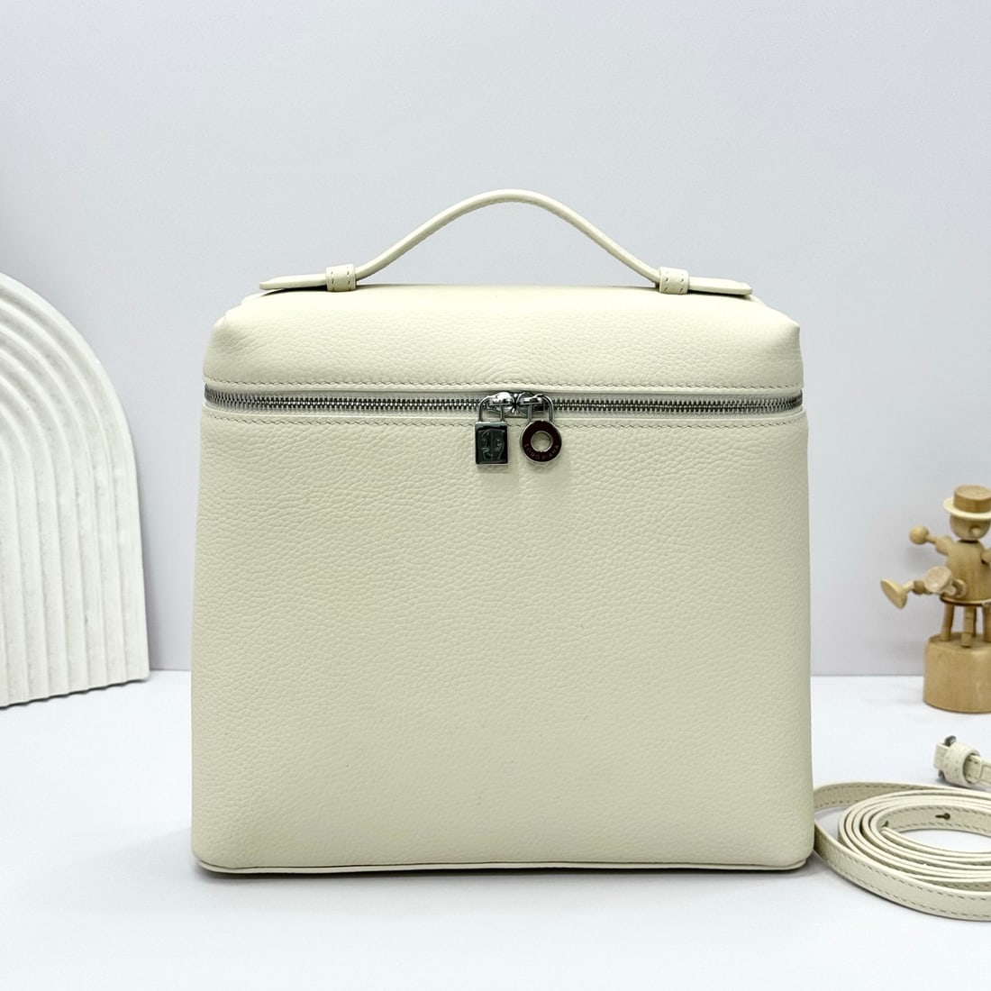 Loropiana Extra Pocket L23.5 Backpack: The Loropiana Extra Pocket L23.5 backpack in a delicate white transforms a minimalist design into a spacious square bag, elongated towards the base. Crafted from calfskin, the subtle hammered texture 