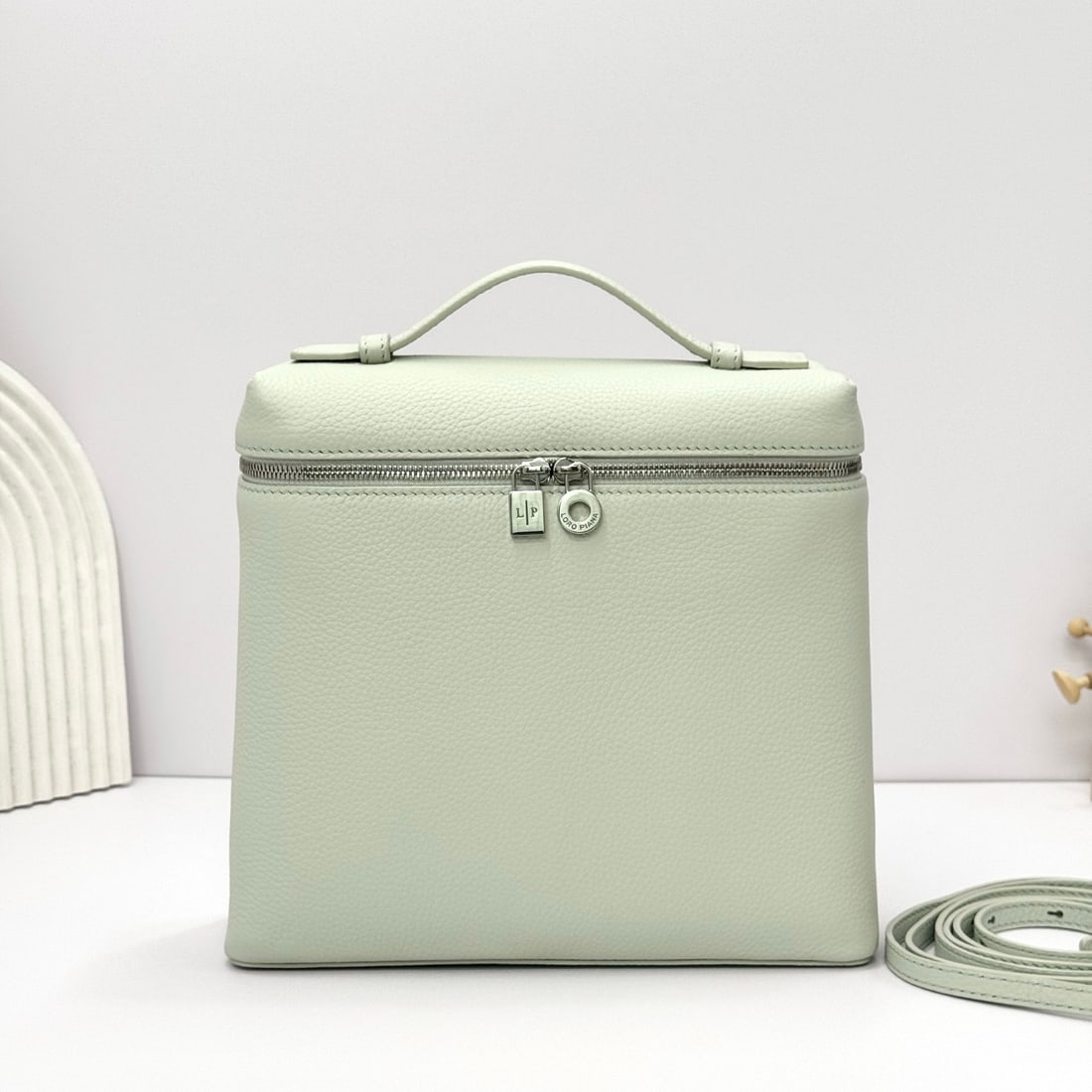 Loropiana Extra Pocket L23.5 Backpack: The Loropiana Extra Pocket L23.5 backpack in a light blue hue transforms a minimalist design into a large-capacity square bag, elongated towards the base. Crafted from calfskin, the subtle hammered te