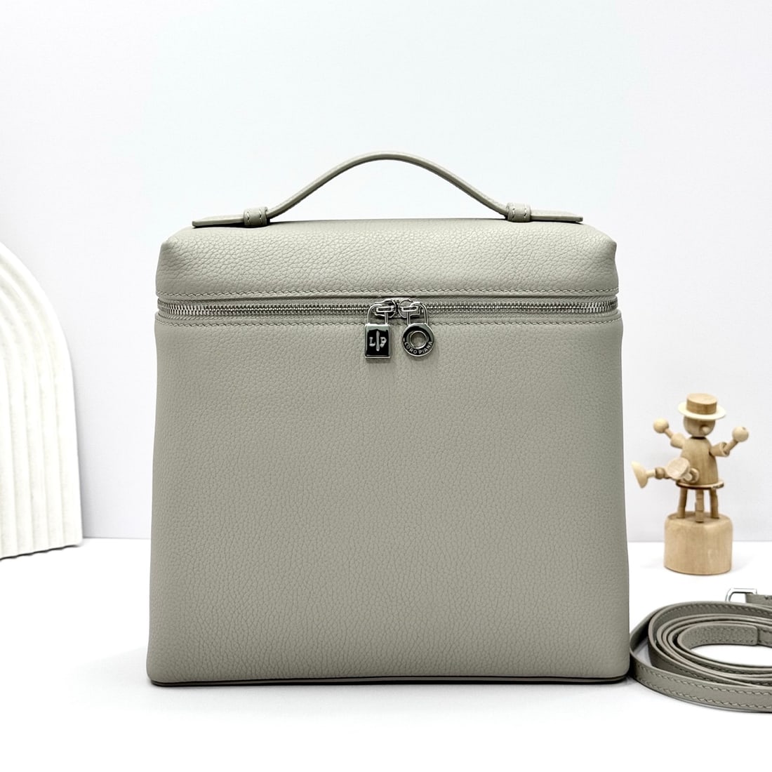 Loropiana Extra Pocket L23.5 Backpack: The Loropiana Extra Pocket L23.5 backpack in pearl gray transforms a minimalist design into a large-capacity square bag, elongated towards the base. Crafted from calfskin, the subtle hammering enhance