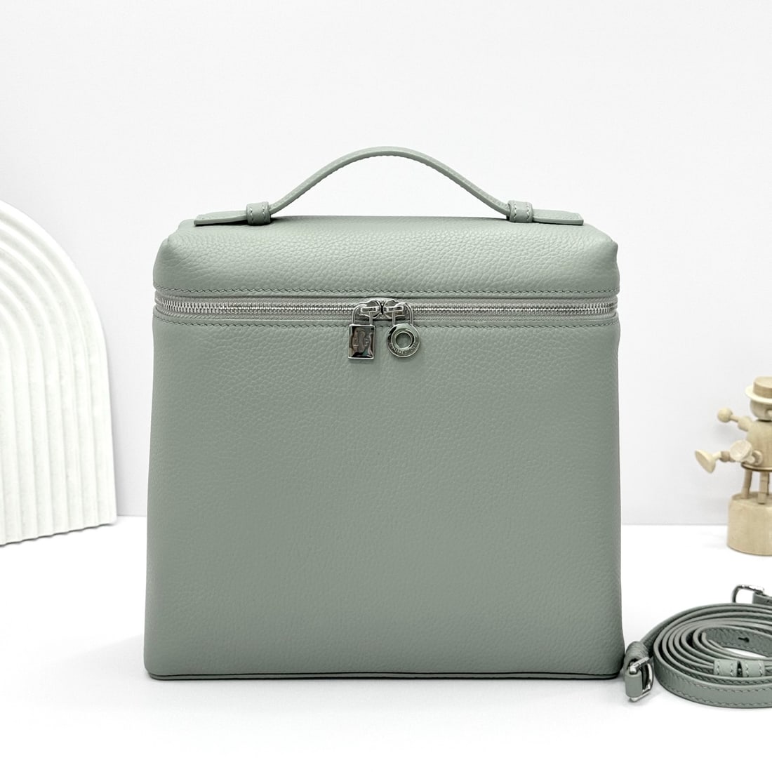 Loropiana Extra Pocket L23.5 Backpack: The Loropiana Extra Pocket L23.5 backpack in a light gray-green hue transforms a minimalist design into a large-capacity square bag, elongated towards the base. Crafted from calfskin, the subtle hamme