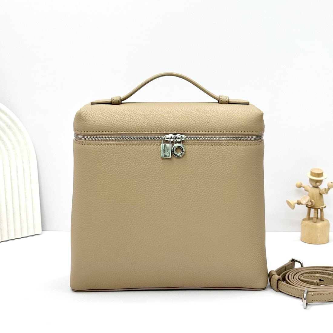 Loropiana Extra Pocket L23.5 Backpack: The Loropiana Extra Pocket L23.5 backpack in a light frankincense color transforms a minimalist design into a large-capacity square bag, elongated towards the base. Crafted from calfskin, the subtle h