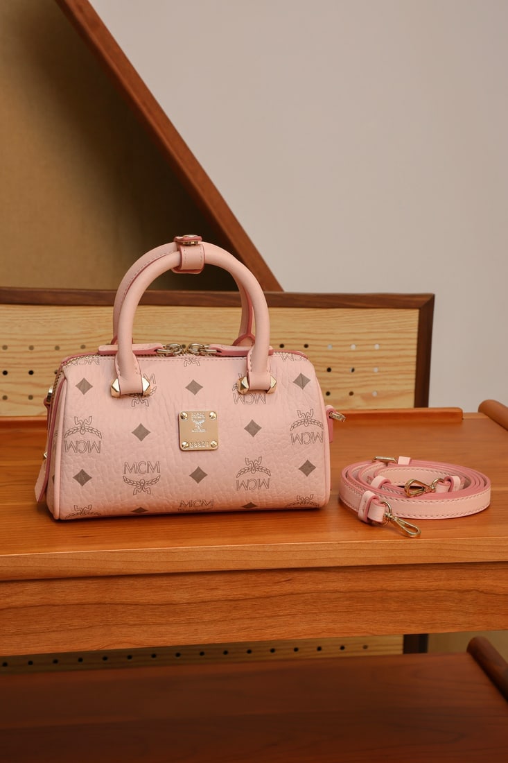 MCM Aren Essential Cherry Blossom Pink Mini Boston Pillow Bag: MCM Aren Essential Cherry Blossom Pink Mini Boston Pillow Bag. A classic cognac-colored bag with an all-over monogram print. Can be worn as a shoulder bag or crossbody. This mini Boston bag offers a f