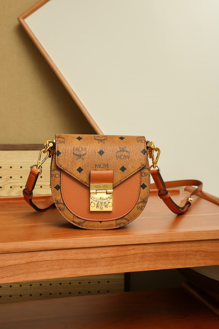 MCM Patricia Visetos Cognac-colored Mini Saddle Crossbody Handbag: MCM Patricia Visetos Cognac Mini Saddle Crossbody Handbag with All-over Monogram Print. Dimensions: 17 x 7 x 17 cm. Shoulder Strap: Adjustable 97-113 cm. Handles: 8 cm long. Closure: Flap. Color: Cogn